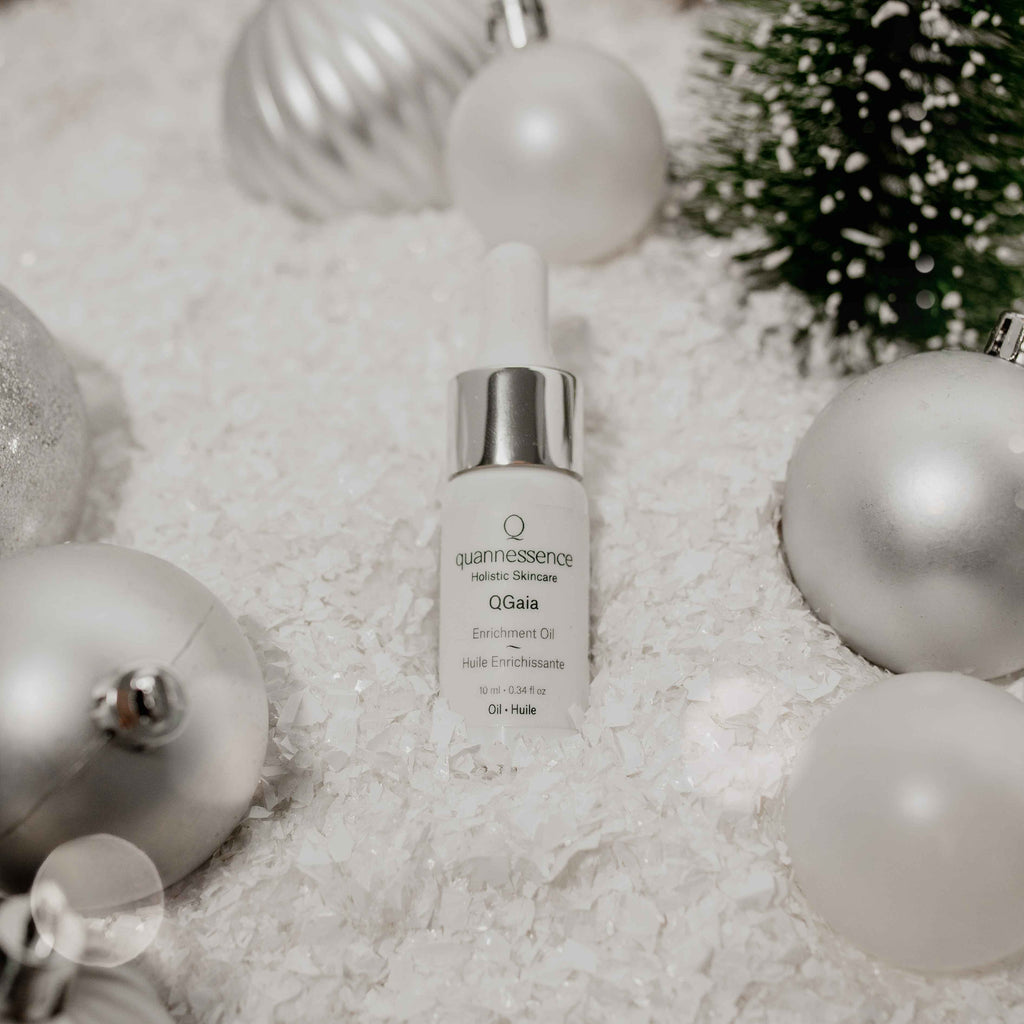 QGaia Skincare serum bottle with Christmas ornaments on a textured surface