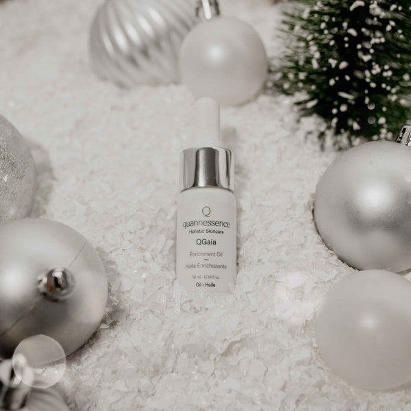 QGaia Skincare serum bottle with Christmas ornaments on a textured surface
