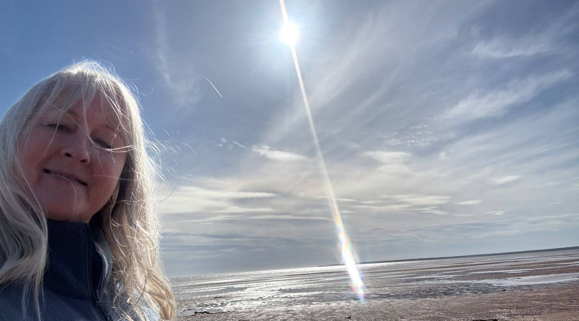 Sharon Quann, founder and ceo of Quannessence Skincare, person with blonde hair standing on a beach with a rainbow in the sky.
