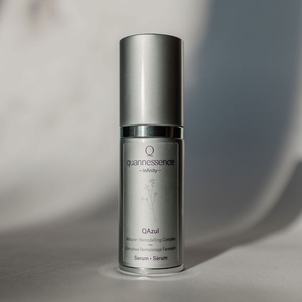 Skincare serum bottle labeled 'quannessence' on a neutral background. Quannessence Skincare, Infinity Collection, professional skincare, Holistic Beauty, Made in Canada, Naturally Sourced, Active ingredients, women-owned, Face, Serums, Qazul, Azul Rejuvenating Serum, Silver packaging with silver lid and pump