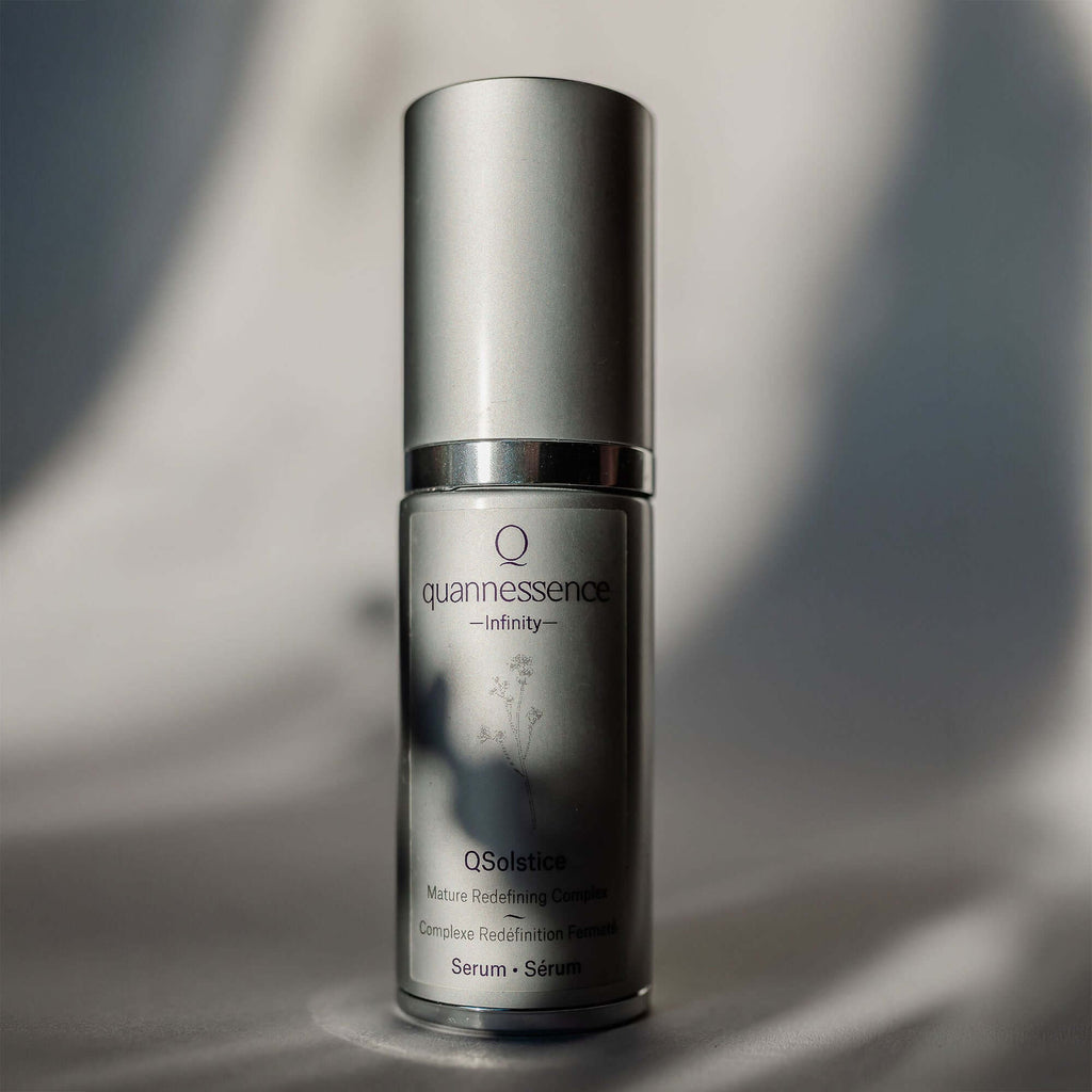 Skincare serum bottle with 'quannessence' branding on a gray background. Quannessence Skincare, Infinity Collection, professional skincare, Holistic Beauty, Made in Canada, Naturally Sourced, Active ingredients, women-owned, Face, Serum, QSolstice, Solstice Redefining Serum, Silver packaging with silver lid and pump