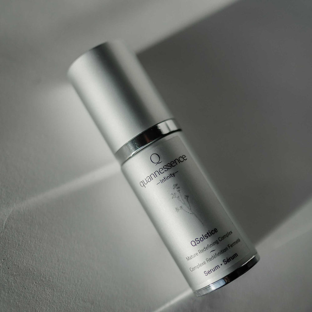 Skincare serum bottle labeled 'quannessence' on a neutral background. Quannessence Skincare, Infinity Collection, professional skincare, Holistic Beauty, Made in Canada, Naturally Sourced, Active ingredients, women-owned, Face, Serum, QSolstice, Solstice Redefining Serum, Silver packaging with silver lid and pump