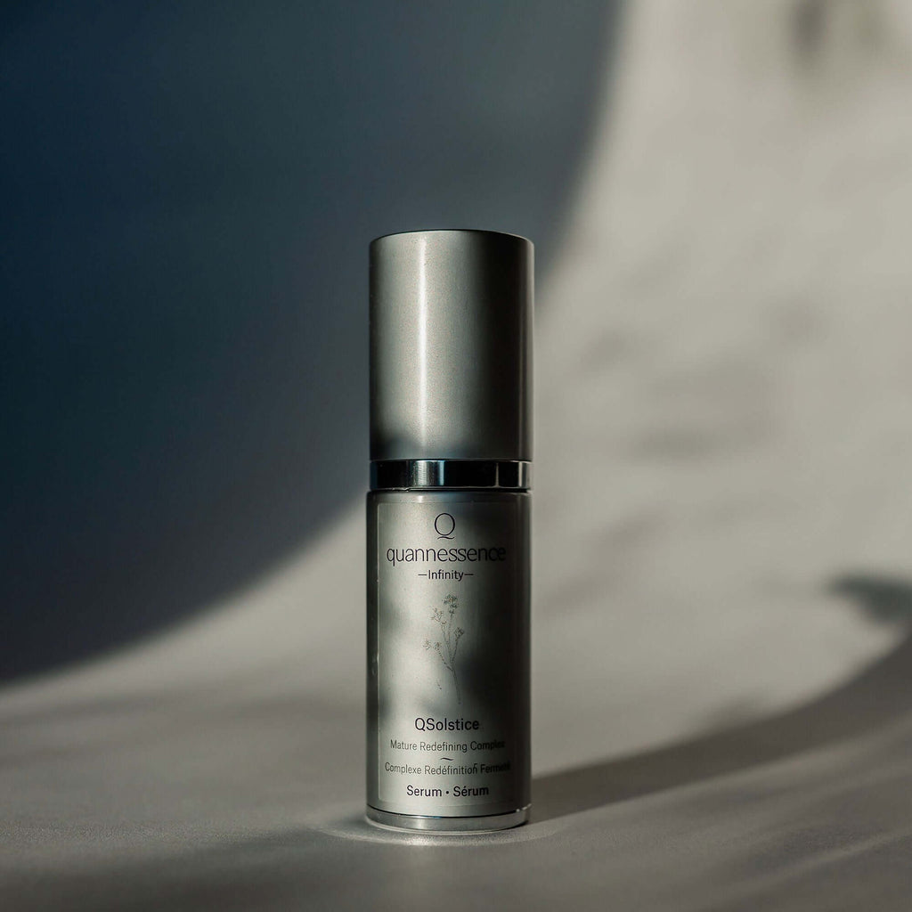 Skincare serum bottle with 'quannessence' branding on a neutral background. Quannessence Skincare, Infinity Collection, professional skincare, Holistic Beauty, Made in Canada, Naturally Sourced, Active ingredients, women-owned, Face, Serum, QSolstice, Solstice Redefining Serum, Silver packaging with silver lid and pump
