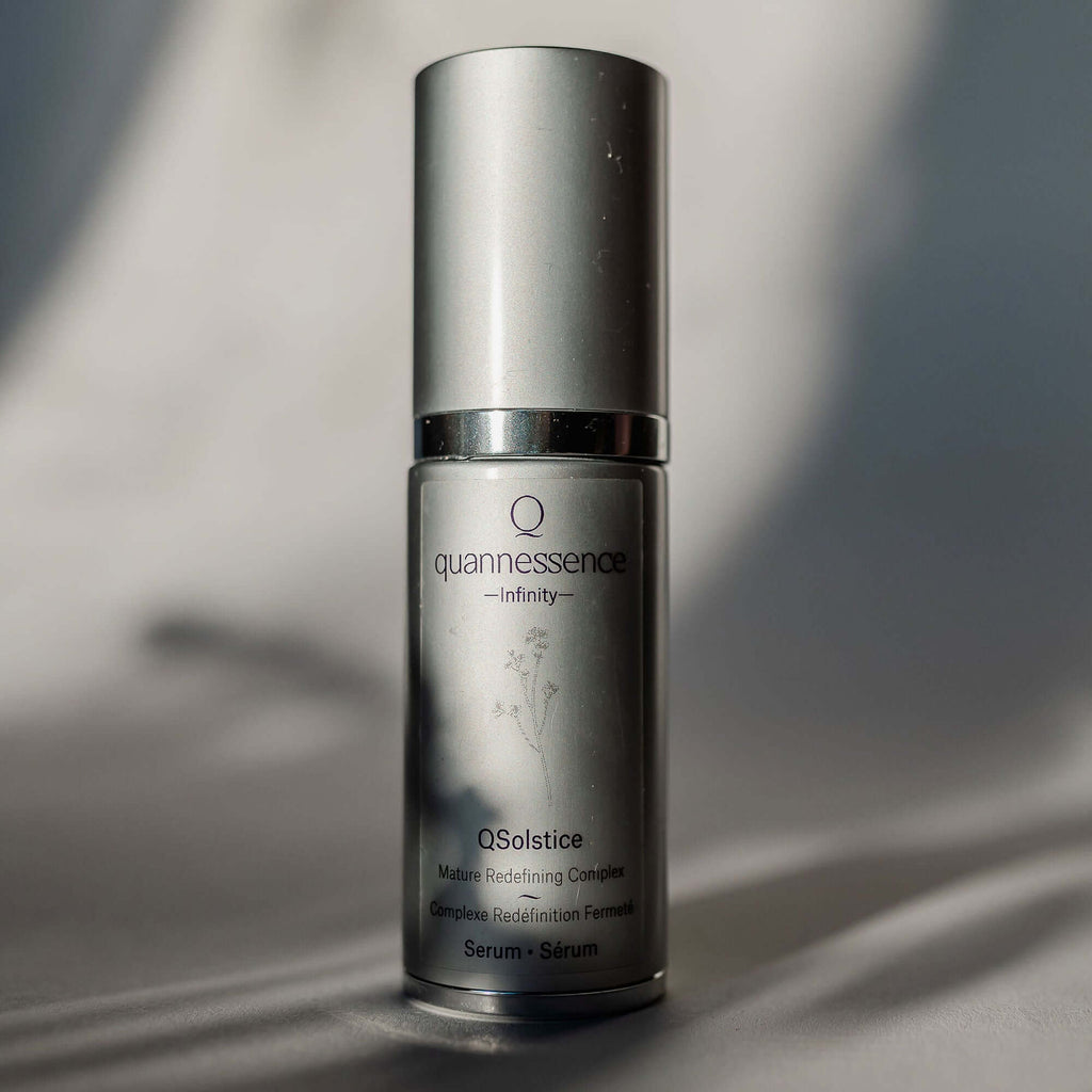 Skincare serum bottle labeled 'quannessence' on a neutral background. Quannessence Skincare, Infinity Collection, professional skincare, Holistic Beauty, Made in Canada, Naturally Sourced, Active ingredients, women-owned, Face, Serum, QSolstice, Solstice Redefining Serum, Silver packaging with silver lid and pump