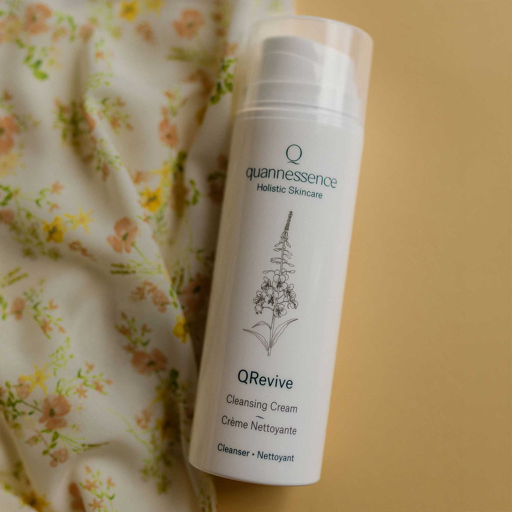 QRevive Cleansing Cream by Quannessence, Quannessence QRevive Cleansing Cream bottle on a floral fabric background. Quannessence QRevive Cleansing Cream bottle with floral elements on a light background. Quannessence Skincare, professional skincare, Holistic Beauty, Made in Canada, Naturally Sourced, Active ingredients, women-owned, Face, Cleanser, Cream, QRevive, Facial Cleansing Cream, white container with pump