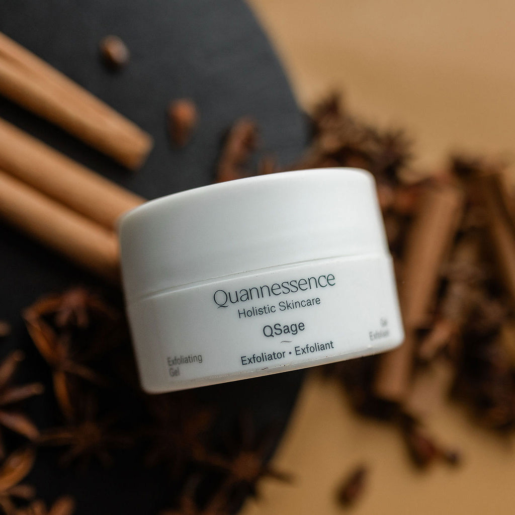 Quannessence Holistic Skincare  jar labeled 'Quannessence' on a textured surface with blurred background