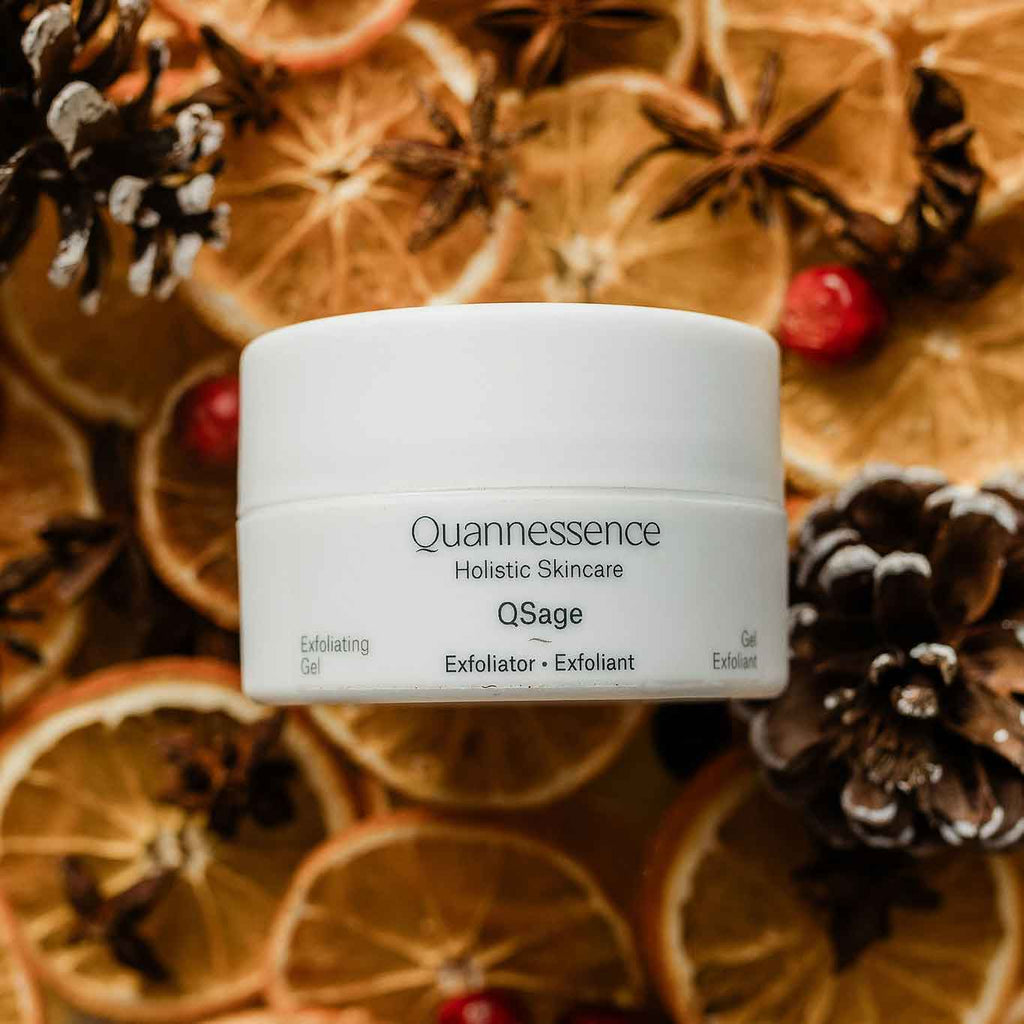Quannessence skincare product on a decorative background with oranges, pine cones, and berries.
