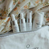 Set of Quannessence skincare products on a floral-patterned fabric background. Quannessence Skincare, professional skincare, Holistic Beauty, Made in Canada, Naturally Sourced, Active ingredients, women-owned, Face, toner, Serum, Oil, QBeauty Sleep, 4-piece kit, white branded cotton travel pouch background