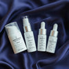 Set of Quannessence skincare products on a textured silky fabric background. Quannessence Skincare, professional skincare, Holistic Beauty, Made in Canada, Naturally Sourced, Active ingredients, women-owned, Face, toner, Serum, Oil, QBeauty Sleep, 4-piece kit, white branded cotton travel pouch