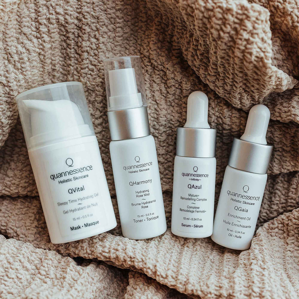 Set of Quannessence skincare products on a textured fabric background. Quannessence Skincare, professional skincare, Holistic Beauty, Made in Canada, Naturally Sourced, Active ingredients, women-owned, Face, toner, Serum, Oil, QBeauty Sleep, 4-piece kit, white branded cotton travel pouch