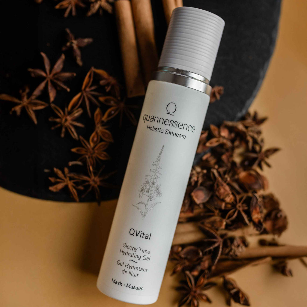Quannessence Holistic Skincare QVital skincare gel bottle on a wooden surface with star anise and cinnamon sticks.