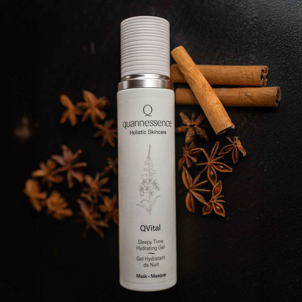 Quannessence Holistic Skincare bottle labeled 'quannessence' with cinnamon sticks and star anise on a dark background