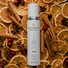 Quannessence Holistic Skincare bottle labelled 'quannessence' on a background of dried oranges, cinnamon sticks, and cranberries.