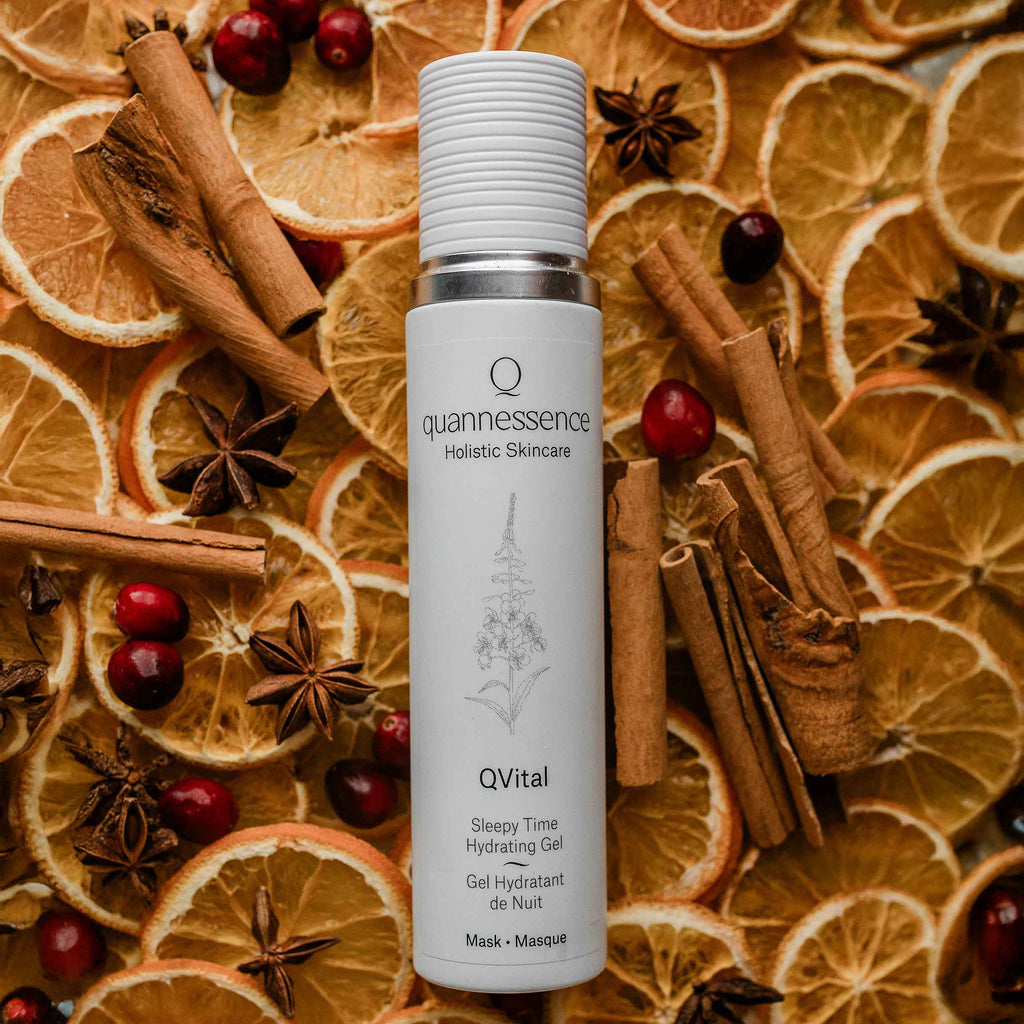 Quannessence Holistic Skincare bottle labelled 'quannessence' on a background of dried oranges, cinnamon sticks, and cranberries.