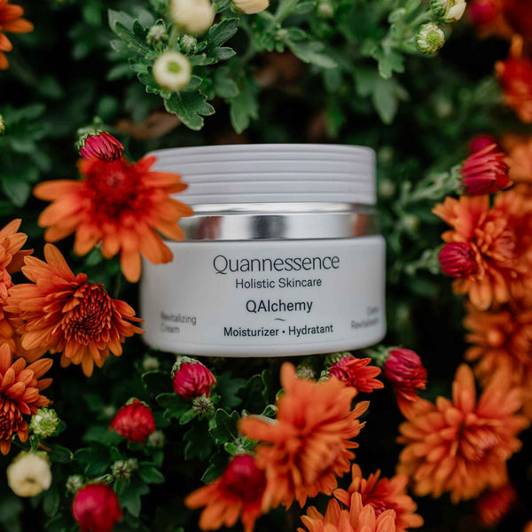 Quannessence skincare jar surrounded by vibrant orange and red flowers. Quannessence Skincare, professional skincare, Holistic Beauty, Made in Canada, Naturally Sourced, Active ingredients, women-owned, Face, Moisturizer, Lotion, Cream, QAlchemy, Alchemist Revitalizing Cream, white jar