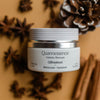 Quannessence Holistic Skincare jar with a blurred background of star anise and cinnamon sticks.