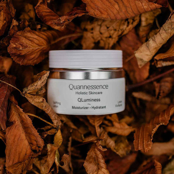 Quannessence skincare product on a bed of dried leaves. Quannessence Skincare, professional skincare, Holistic Beauty, Made in Canada, Naturally Sourced, Active ingredients, women-owned, Face, Moisturizer, Lotion, Cream, QLuminess, Luminess Face Lotion, white jar