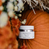 Quannessence skincare jar with pumpkins and flowers in the background. Quannessence Skincare, professional skincare, Holistic Beauty, Made in Canada, Naturally Sourced, Active ingredients, women-owned, Face, Moisturizer, Lotion, Cream, QNourish, uniQue encapsulated Vitamin Lotion, white jar, hand with cream