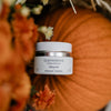 Skincare jar labeled 'Quannessence' on a pumpkin with flowers in the background. Quannessence Skincare, professional skincare, Holistic Beauty, Made in Canada, Naturally Sourced, Active ingredients, women-owned, Face, Moisturizer, Lotion, Cream, QNourish, uniQue encapsulated Vitamin Lotion, white jar, hand with cream