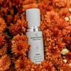 Skincare bottle labeled 'quannessence' on a bed of orange flowers. Quannessence Skincare, professional skincare, Holistic Beauty, Made in Canada, Naturally Sourced, Active ingredients, women-owned, Face, Oil, All Natural, QGaia, Gaia Facial Enrichment Oil, white glass packaging with white lid & pump