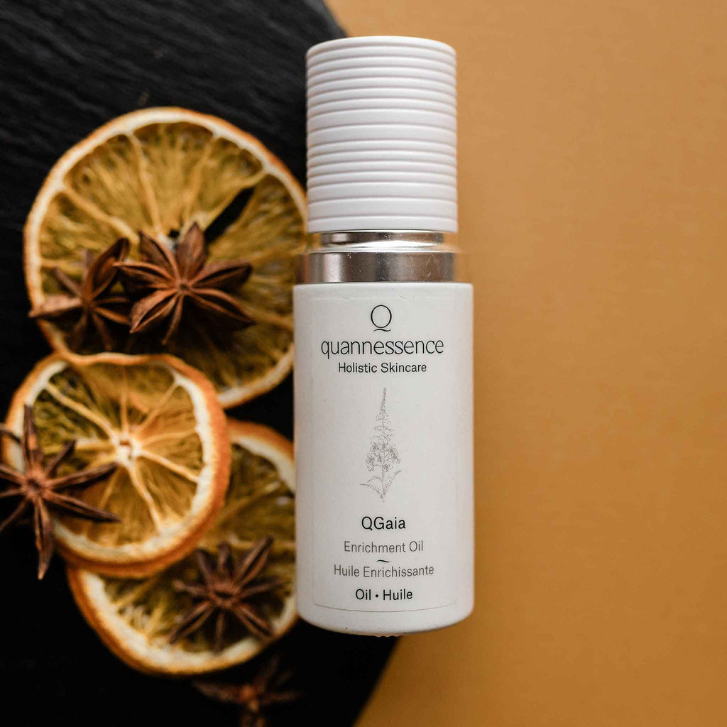 Quannessence Holistic Skincare bottle labeled 'quannessence' with dried oranges and star anise on a dark surface.