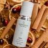 Quannessence Holistic Skincare bottle labeled 'quannessence' on a background of cinnamon sticks and oranges.