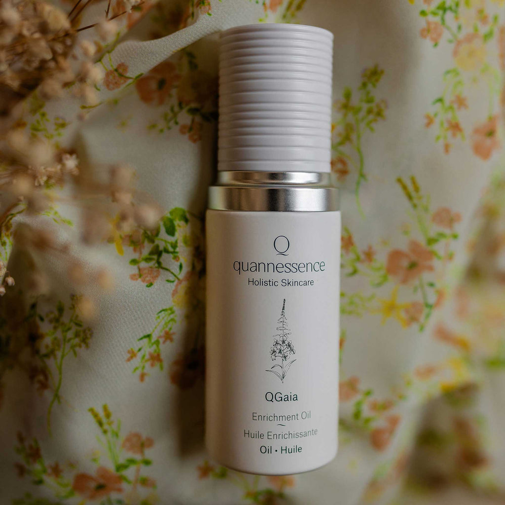 QGaia Enrichment Oil, Skincare bottle labeled 'quannessence' on a floral background. Skincare bottle labeled 'quannessence' on a bed of orange flowers. Quannessence Skincare, professional skincare, Holistic Beauty, Made in Canada, Naturally Sourced, Active ingredients, women-owned, Face, Oil, All Natural, QGaia, Gaia Facial Enrichment Oil, white glass packaging with white lid & pump