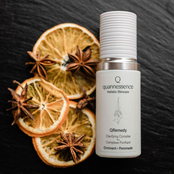 Quannessence Holistic Skincare bottle labelled 'quannessence' with dried oranges and star anise on a dark background