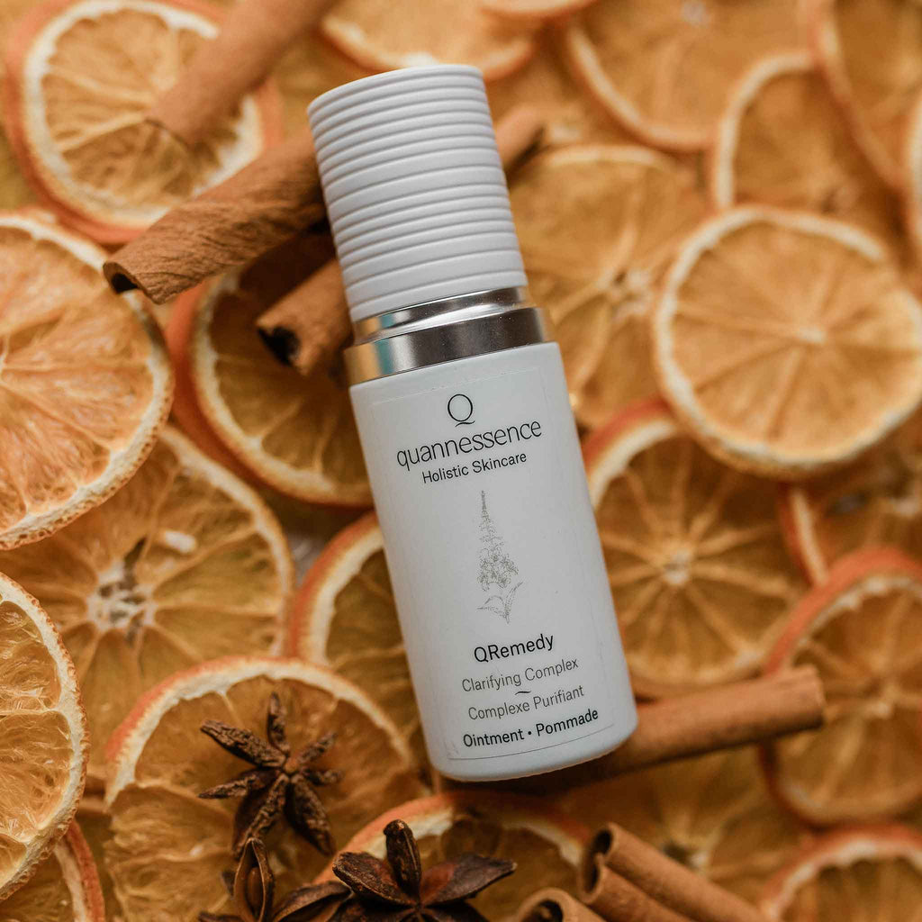 Quannessence Holistic Skincare  bottle labeled 'quannessence' on a background of dried oranges and cinnamon sticks.