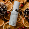 Quannessence Holistic Skincare serum bottle labelled 'quan nessence' on a decorative background with dried oranges and pine cones.