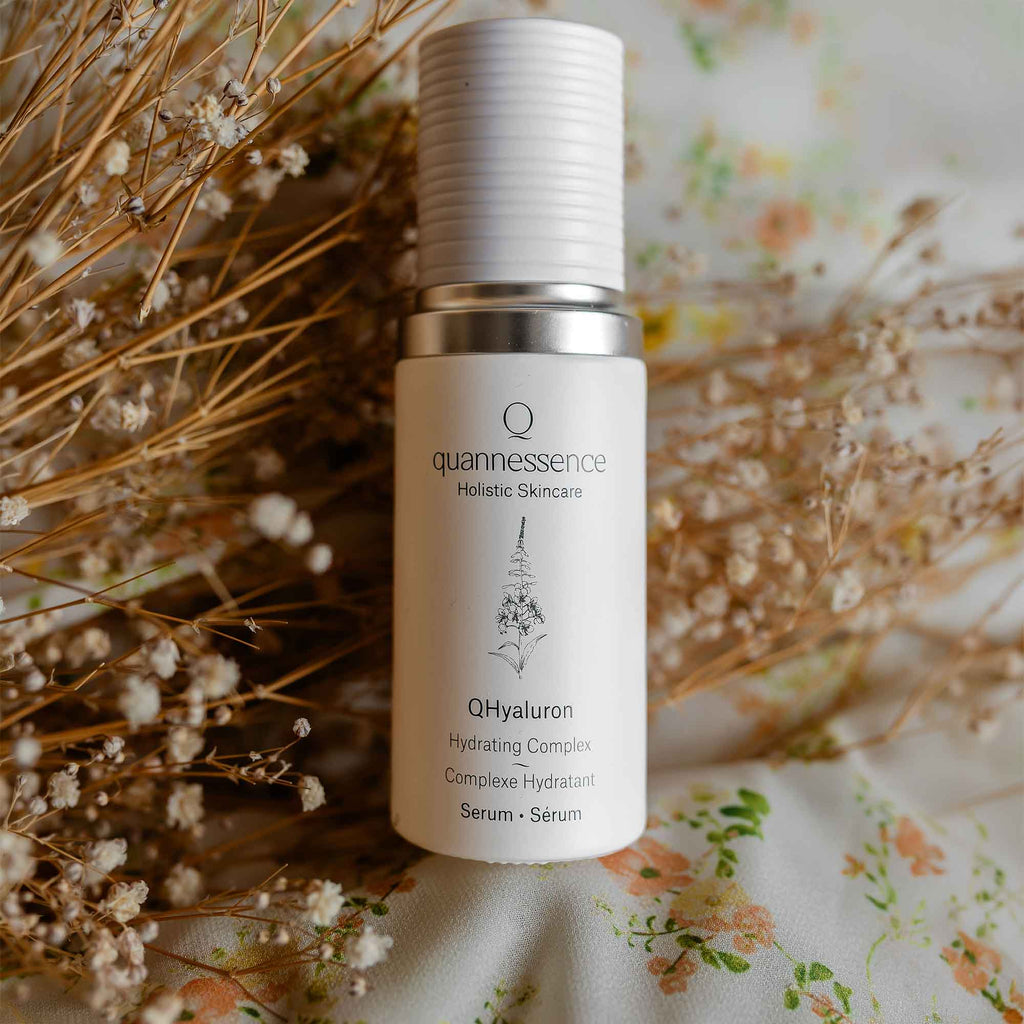 QHyaluron Hydrating Complex by Quannessence, Skincare serum bottle with 'quannessence' branding on a floral background. Quannessence Skincare, professional skincare, Holistic Beauty, Made in Canada, Naturally Sourced, Active ingredients, women-owned, Face, Serum, QHYaluron, Hyaluronic (PUR) Hydrating Serum, white glass packaging with white lid & pump