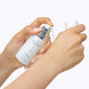 Person applying a droplet of a white serum bottle labeled 'quannessence' to their skin. Quannessence Skincare, professional skincare, Holistic Beauty, Made in Canada, Naturally Sourced, Active ingredients, women-owned, Face, Serum, QHYaluron, Hyaluronic (PUR) Hydrating Serum, white glass packaging with white lid & pump