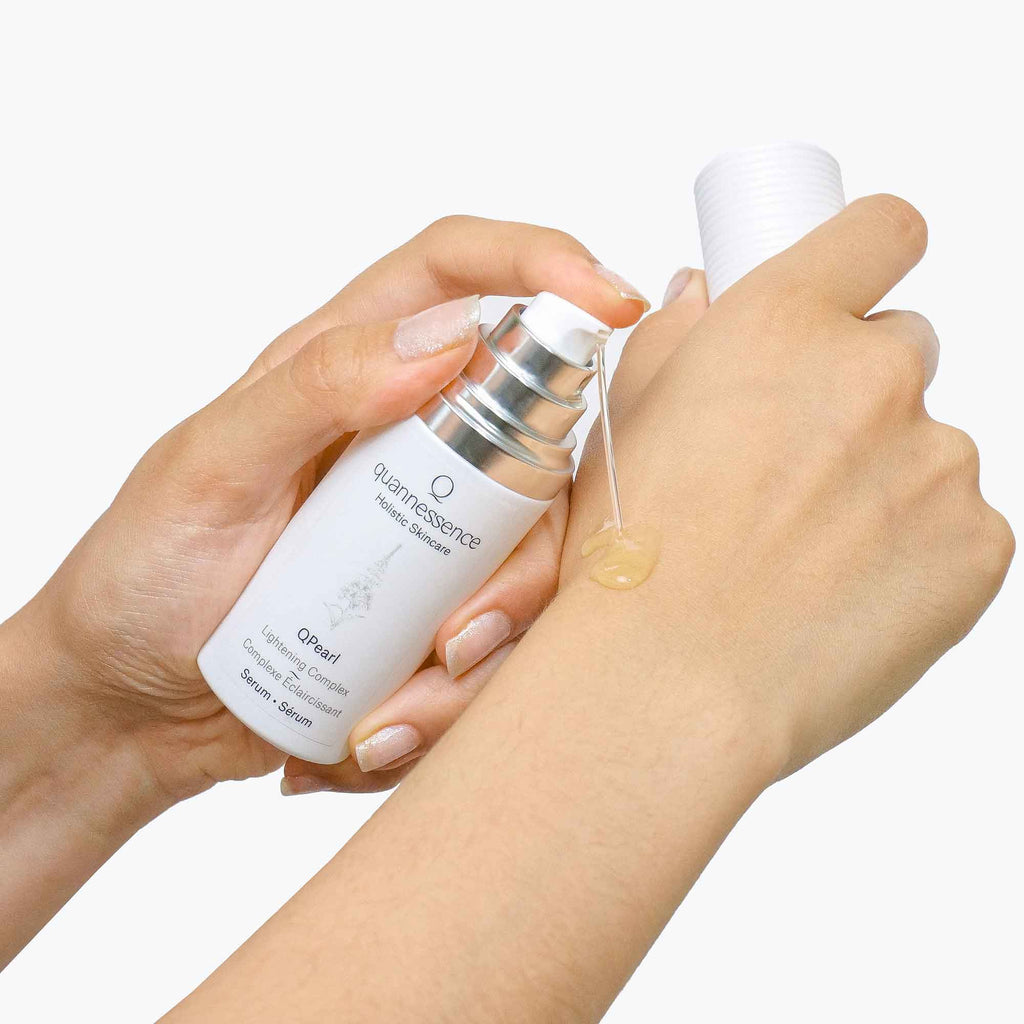 Person holding a skincare bottle and applying product to their hand against a white background. Quannessence Skincare, professional skincare, Holistic Beauty, Made in Canada, Naturally Sourced, Active ingredients, women-owned, Face, Serum, QPearl, Pearlessence Brightening Gel, white glass packaging with white lid & pump