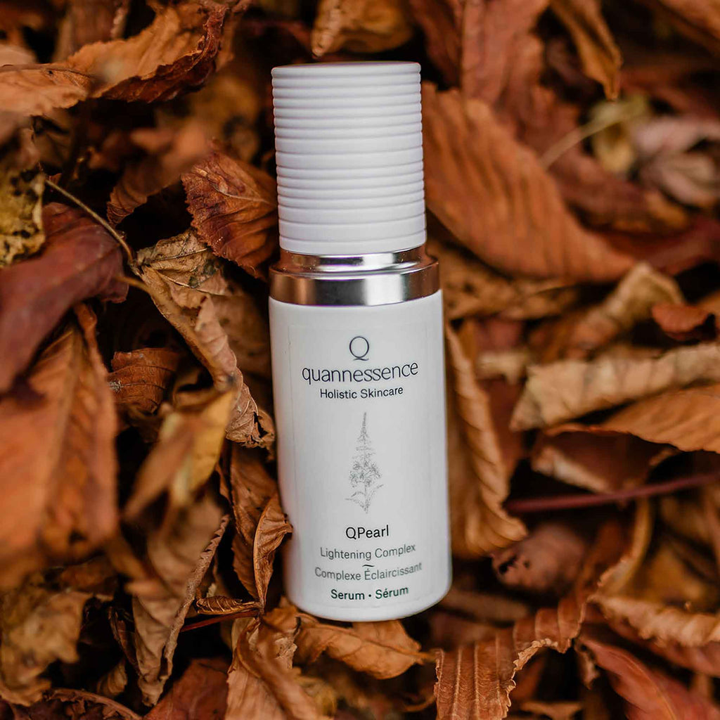 Skincare serum bottle labeled 'quannessence' on a background of dried leaves. Quannessence Skincare, professional skincare, Holistic Beauty, Made in Canada, Naturally Sourced, Active ingredients, women-owned, Face, Serum, QPearl, Pearlessence Brightening Gel, white glass packaging with white lid & pump