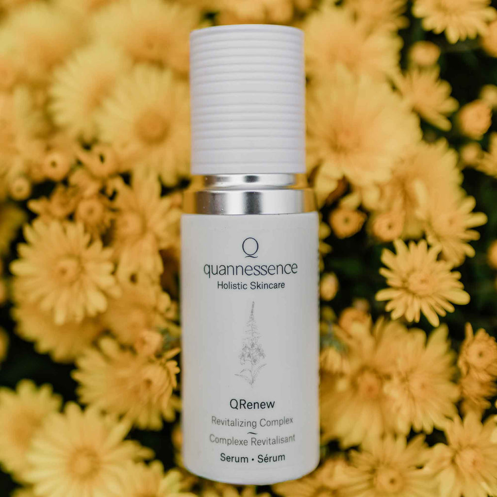 Skincare serum bottle with 'quannessence' branding against a yellow flower background. Quannessence Skincare, professional skincare, Holistic Beauty, Made in Canada, Naturally Sourced, Active ingredients, women-owned, Face, Serum, QFirm, IQ FIRMING GEL, white glass packaging with white lid & pump