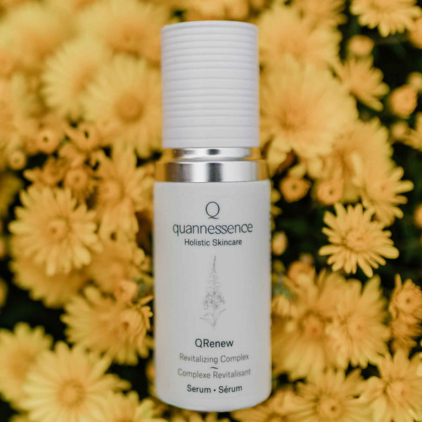 Skincare serum bottle with 'quannessence' branding against a yellow flower background. Quannessence Skincare, professional skincare, Holistic Beauty, Made in Canada, Naturally Sourced, Active ingredients, women-owned, Face, Serum, QFirm, IQ FIRMING GEL, white glass packaging with white lid & pump