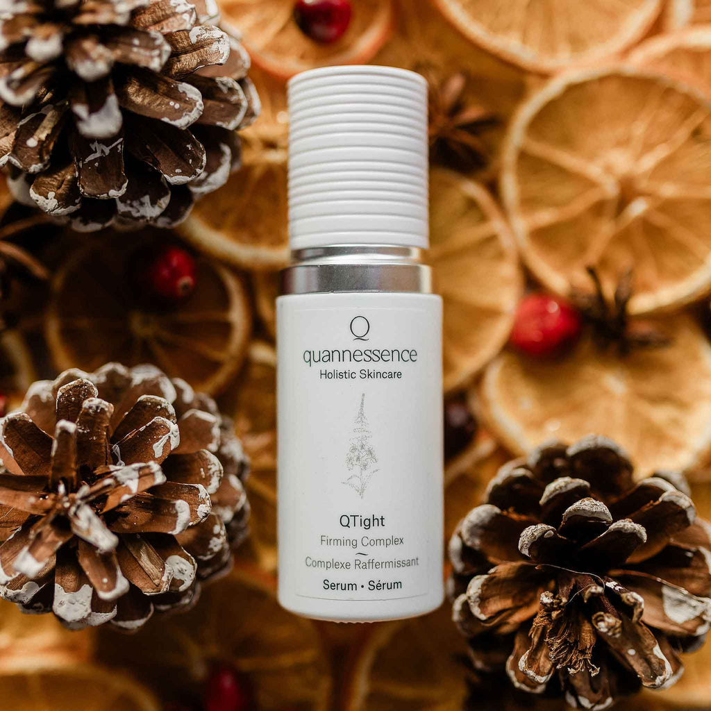 Quannessence Holistic Skincare serum bottle with decorative pinecones and oranges in the background