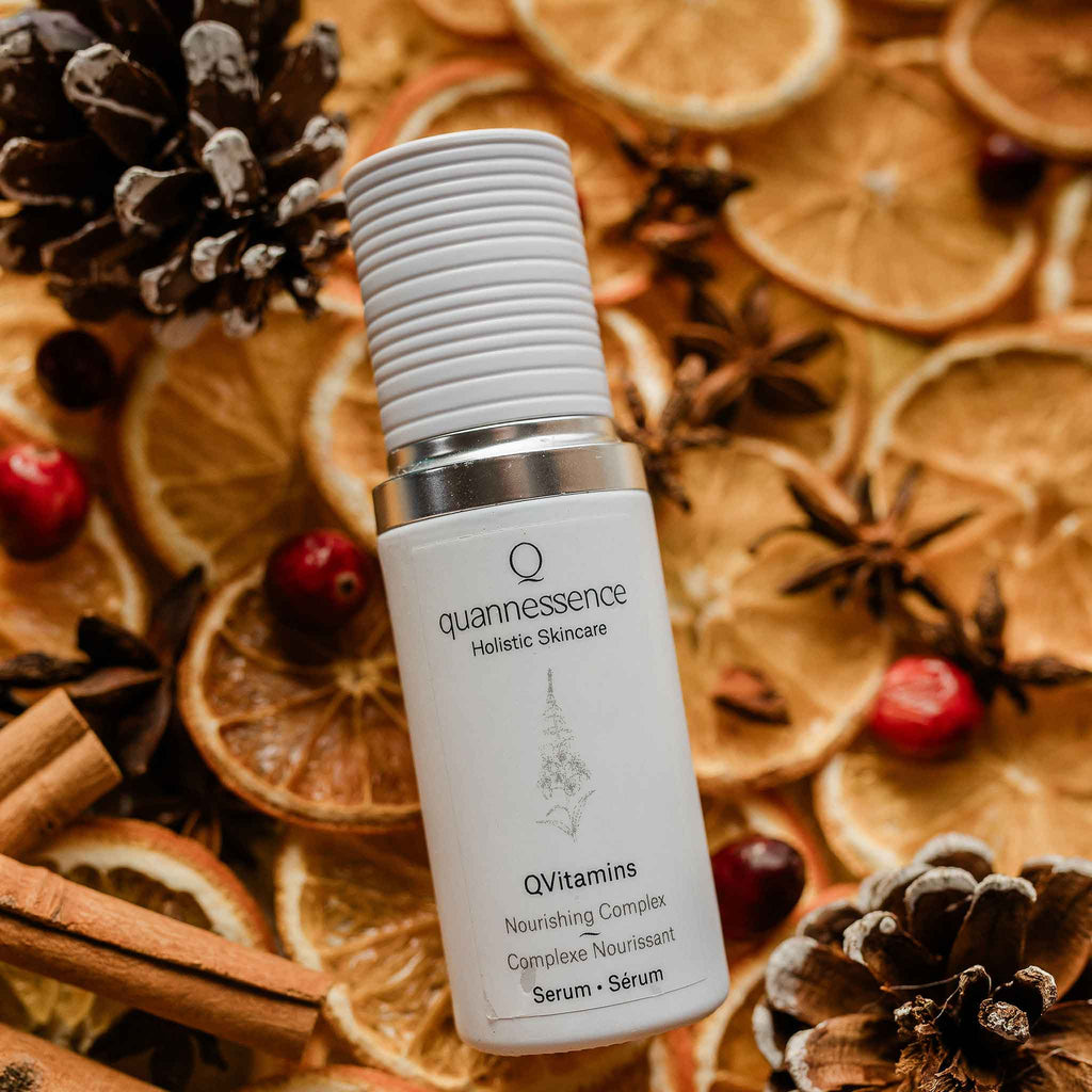 Quannessence Holistic Skincare serum bottle labeled 'quannessence' on a decorative background with dried oranges, pine cones, and cinnamon sticks.